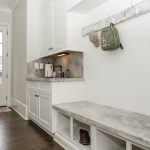custom-designed mudroom with white cabinets separate sink and hooks for coats