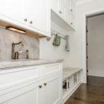 custom-designed mudroom with white cabinets separate sink and hooks for coats