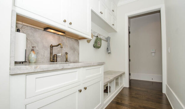 custom-designed mudroom with white cabinets separate sink and hooks for coats