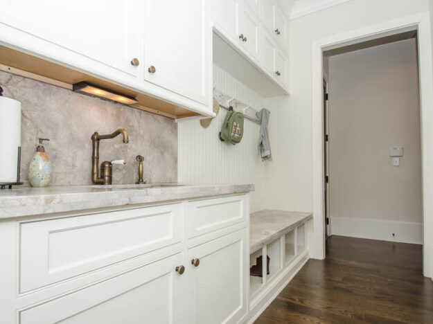 custom-designed mudroom with white cabinets separate sink and hooks for coats