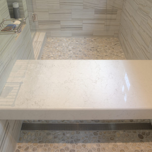 close up of shower bench in large walk-in shower with river rock flooring