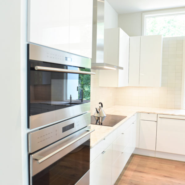 modern Atlanta white kitchen design featuring island with waterfall edge luxury appliances and contemporary pendant light fixtures
