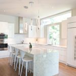 modern Atlanta white kitchen design featuring island with waterfall edge luxury appliances and contemporary pendant light fixtures