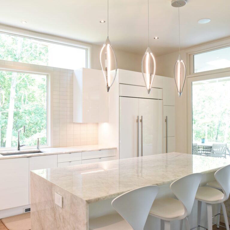 modern Atlanta white kitchen design featuring island with waterfall edge luxury appliances and contemporary pendant light fixtures
