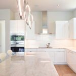 modern Atlanta white kitchen design featuring island with waterfall edge luxury appliances and contemporary pendant light fixtures