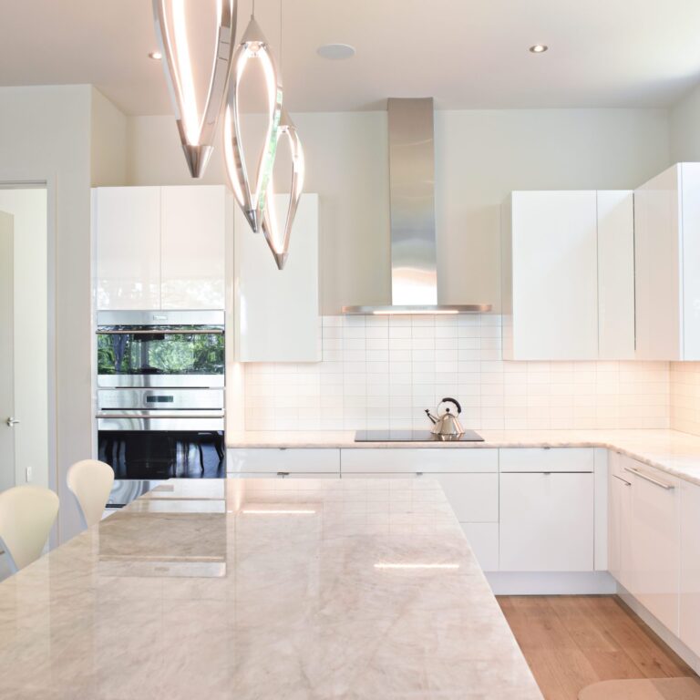 modern Atlanta white kitchen design featuring island with waterfall edge luxury appliances and contemporary pendant light fixtures