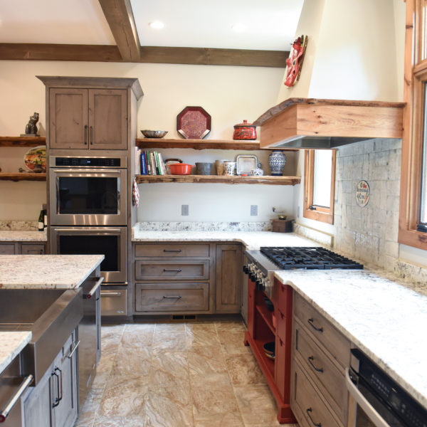 rustic kitchen renovation with custom grey cabinets large island with seating for four red pops of color on accent cabinets floating shelves exposed beams