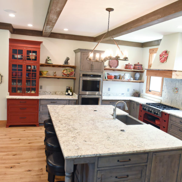 rustic kitchen renovation with custom grey cabinets large island with seating for four red pops of color on accent cabinets floating shelves exposed beams