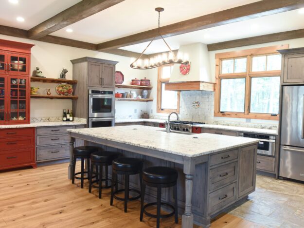 rustic kitchen renovation with custom grey cabinets large island with seating for four red pops of color on accent cabinets floating shelves exposed beams