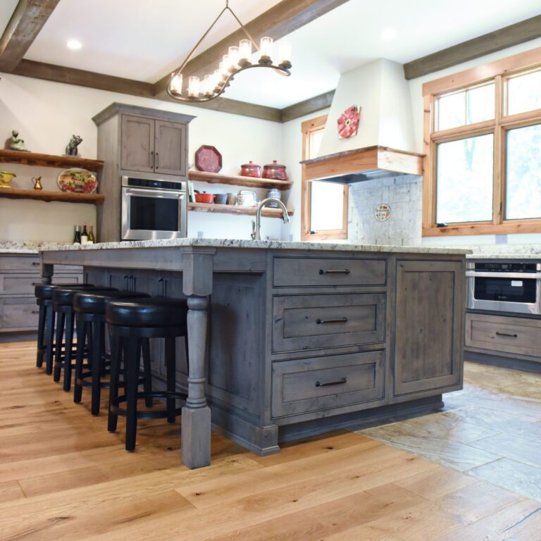 rustic kitchen renovation with custom grey cabinets large island with seating for four red pops of color on accent cabinets floating shelves exposed beams