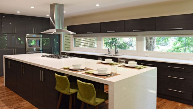 this modern Atlanta kitchen renovation features a large island, custom dark cabinets, luxury appliances and lots of windows looking into the wooded yard