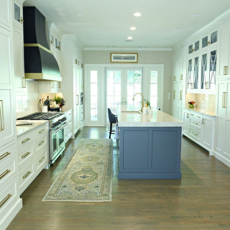 picture of beautiful kitchen renovation in buckhead with large blue island and white upper and lower cabinets with black vent hood and luxury appliances with brass hardware and trim
