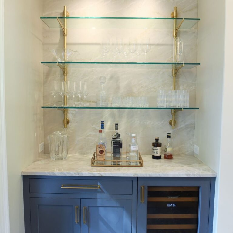 picture of a custom bar with a blue base cabinet and a quartzite top with glass shelves mounted with brass hardware