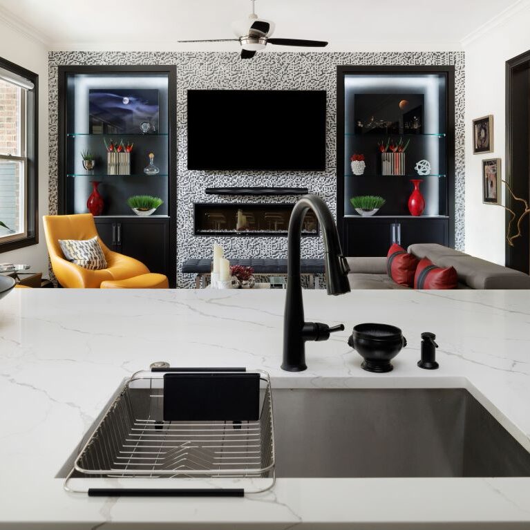 The kitchen island in this renovated Alpharetta townhome overlooks the living room which features black built-in cabinets and uses the same accent tile as in the kitchen
