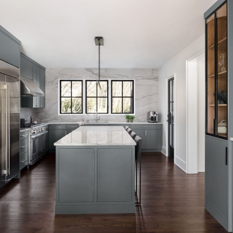wide shot of modern buckhead kitchen renovation showing large island with seating for four and built-in china cabinet as well as overall kitchen layout to sink on rear wall with three windows with black frames
