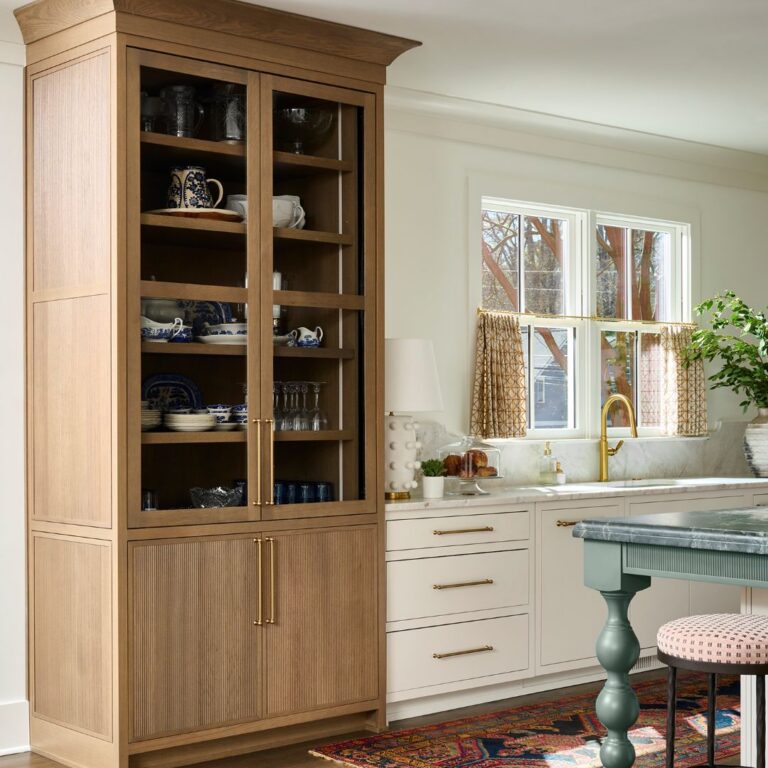 Atlanta kitchen renovation with custom glass-front wood cabinetry, white shaker cabinets, brass hardware, green island with turned legs, and layered transitional design details