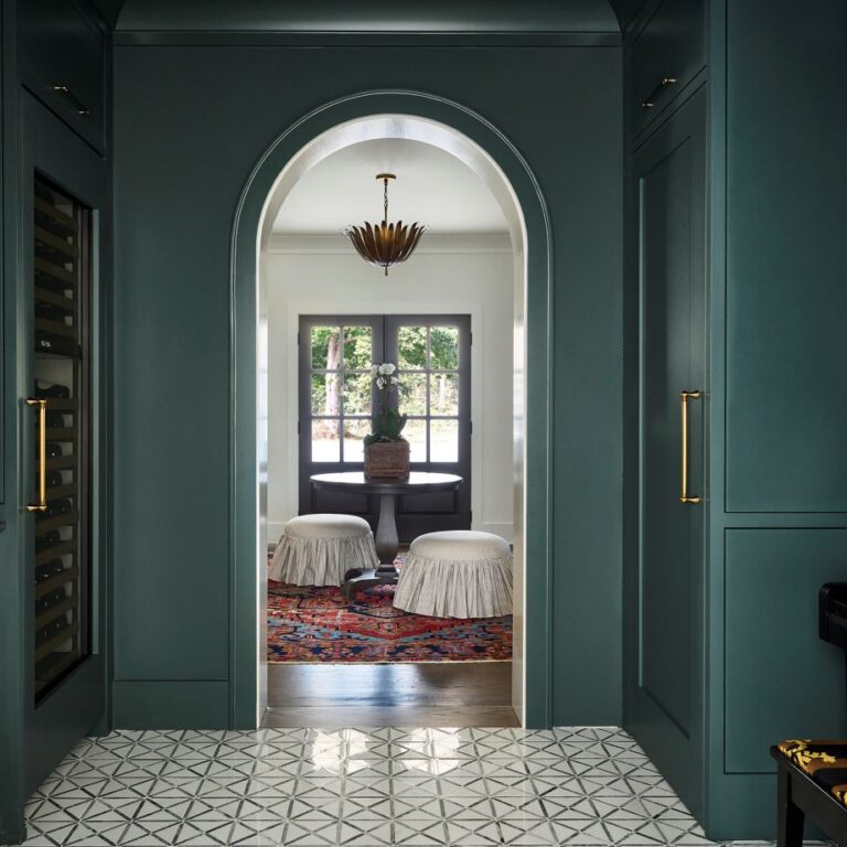 Atlanta home bar and wine storage area featuring dark green custom cabinetry, brass hardware, geometric tile flooring, arched doorway, and moody transitional design details