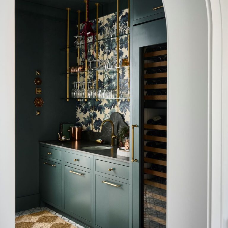 Custom Atlanta bar area featuring dark green cabinetry, brass hardware, floating glass shelves, patterned wallpaper, built-in wine storage, and an arched entryway with dramatic moody design details