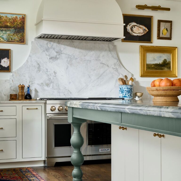 Custom Atlanta kitchen featuring a marble range backsplash, sculpted white vent hood, green furniture-style island, brass accents, Wolf range, and layered traditional details with collected artwork
