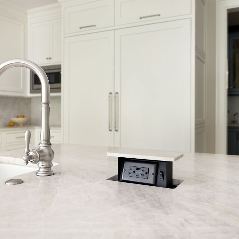 Pop-up electrical outlet built into quartzite kitchen island beside sink and polished nickel faucet