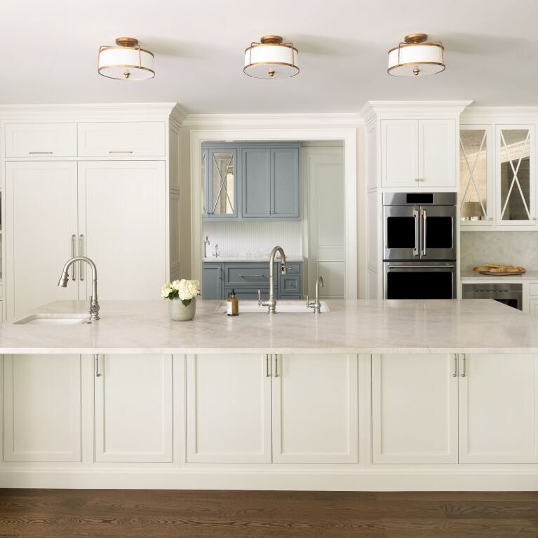 Front view of spacious white kitchen with quartzite island and separate blue-gray beverage center