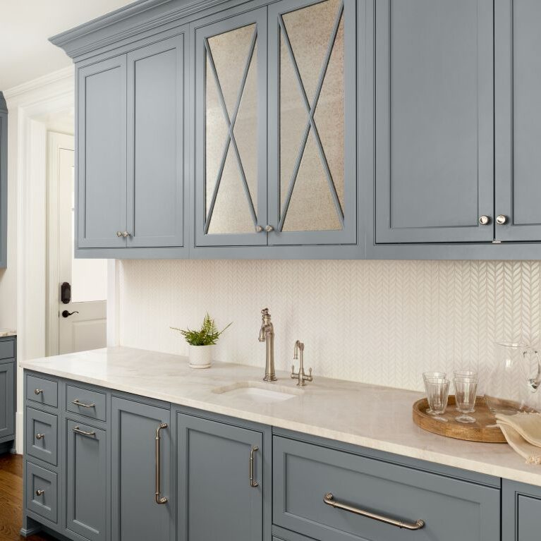 Blue-gray beverage and prep area with mirrored cabinet doors, sink and patterned backsplash