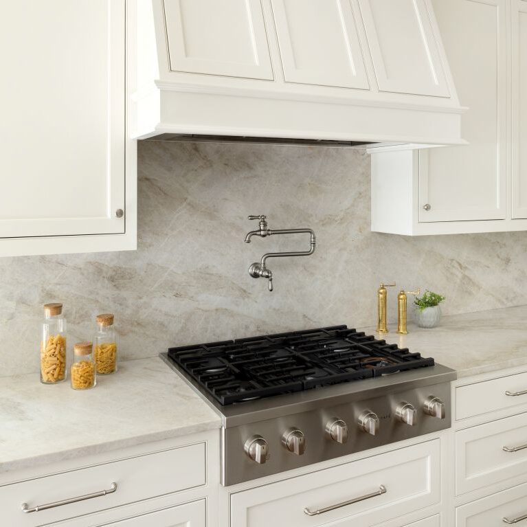 Stainless steel cooktop with pot filler, custom white hood and Taj Mahal quartzite backsplash