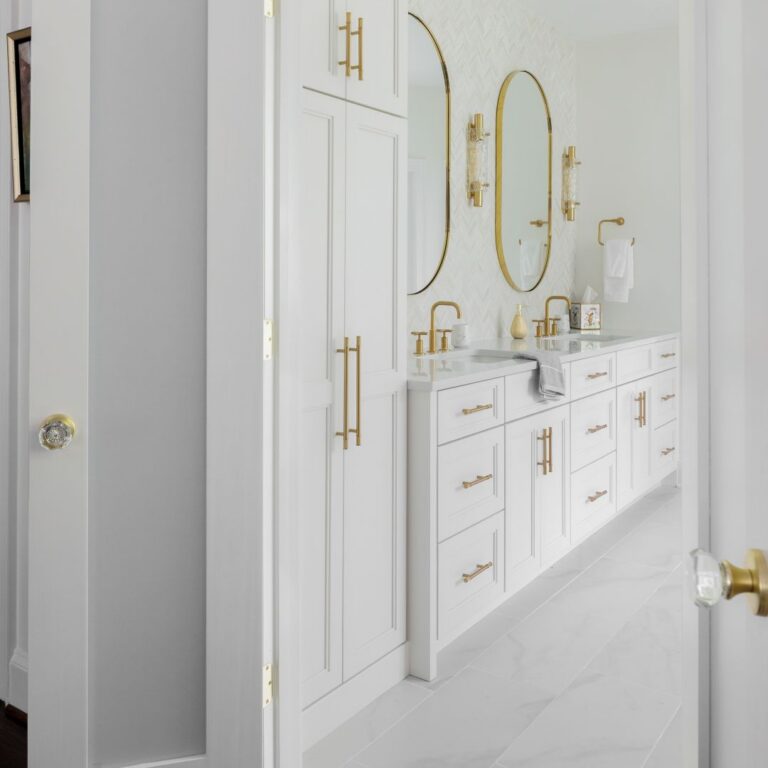 Entrance to renovated Roswell primary bathroom with white double vanity, linen tower, and brushed-gold hardware