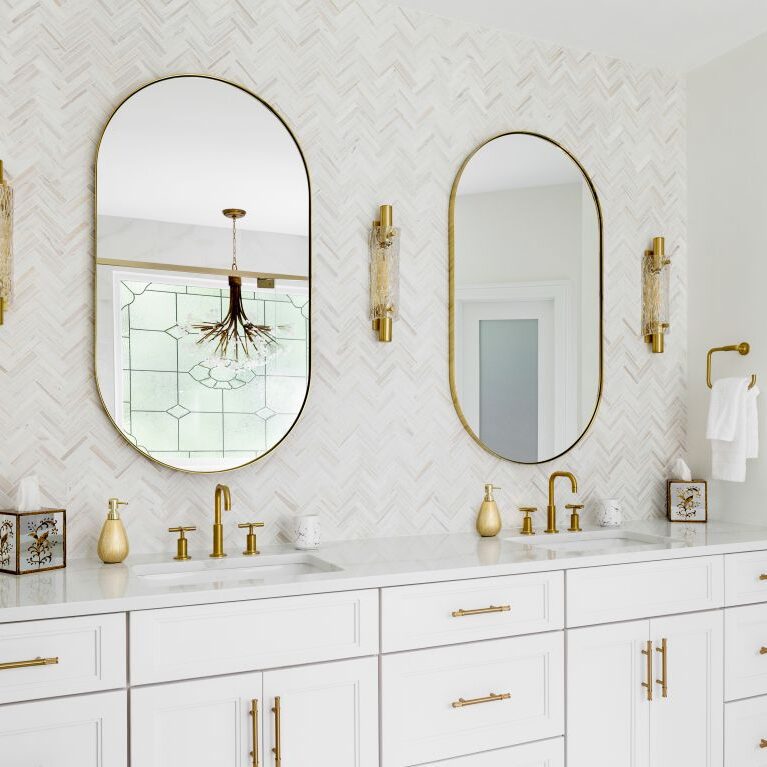 Custom white double vanity with quartz countertop, arched mirrors, and brushed-gold fixtures