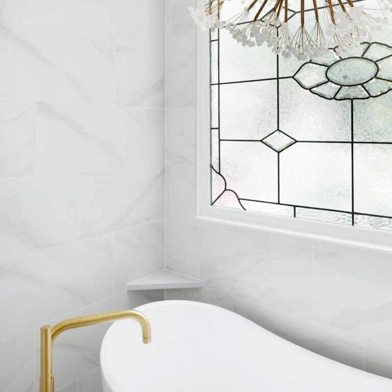 Freestanding soaking tub beneath a decorative-glass window and sculptural chandelier
