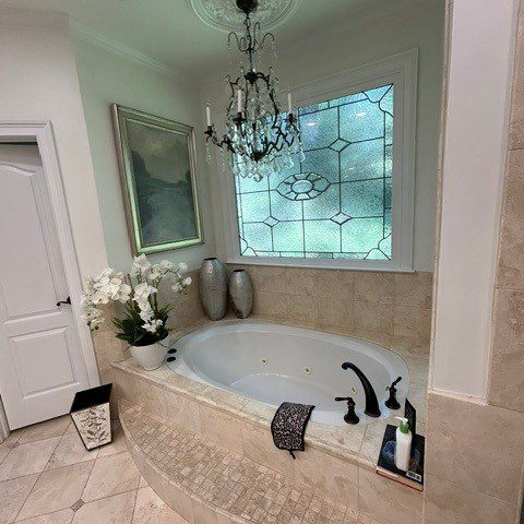 Built-in jetted tub beneath a decorative-glass window and traditional chandelier in the original Roswell bathroom